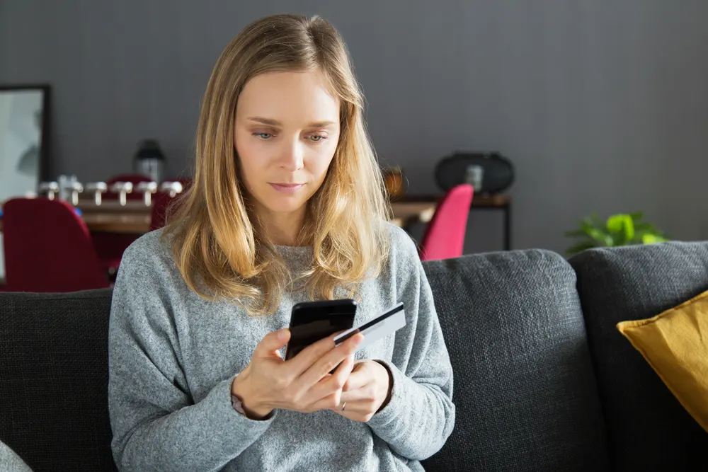 Frau sitzt auf dem Sofa und nutzt Onlinebanking auf dem Smartphone