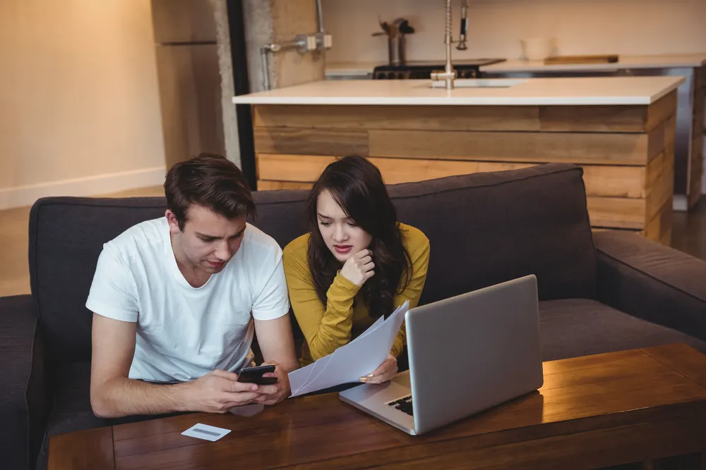 Paar sitzt auf dem Sofa und bespricht Unterlagen am Laptop